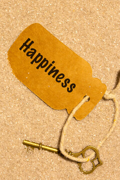 Old vintage key in sand with a card label with the word happiness. Phrase 'key to happiness' concept