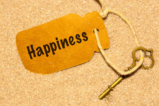 Old vintage key in sand with a card label with the word happiness. Phrase 'key to happiness' concept