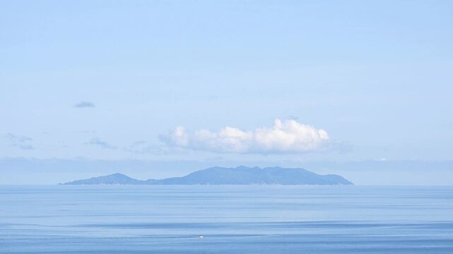 Distant view of Koh Racha Yai Island rising above calm blue waters of the Andaman Sea beneath soft white clouds and a clear blue sky near Rawai Phuket Thailand
