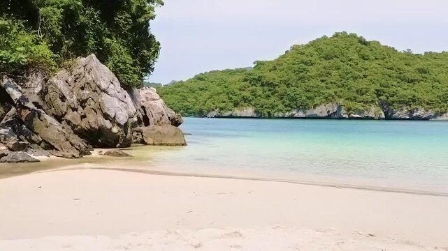 Scenic crescent beach featuring fine white sand and rugged coastal rocks with lush green tropical hills surrounding calm turquoise waters beneath a clear sky in Tri Trang Beach Phuket Thailand