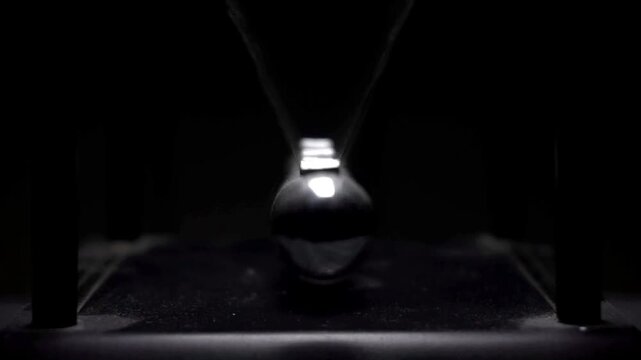 A polished metal sphere swings toward and away from the camera in front of the aligned balls of a Newton cradle against a dark background.