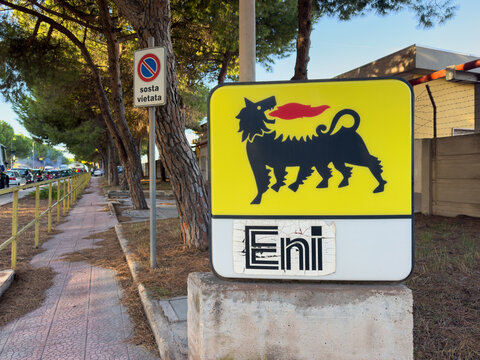 Eni sign beside a pine-lined sidewalk in daylight