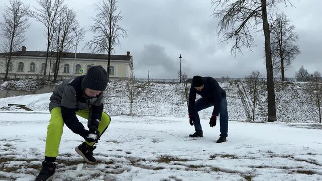 Amidst the white-covered landscape of a park, a father and son share laughter while making a snowman and promptly starting a friendly snowball war.