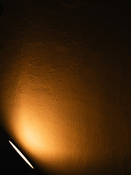 Warm golden spotlight glowing on a dark textured plaster wall with rough surface and a thin crack, moody low-key light and shadow background with copy space