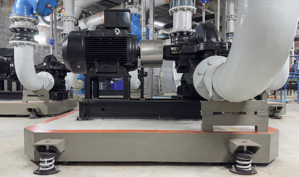 Industrial electric motor connected to water centrifugal pump with heavy pipeline system in building mechanical room. Engineering, plumbing, chiller plant, HVAC utility technology concept.