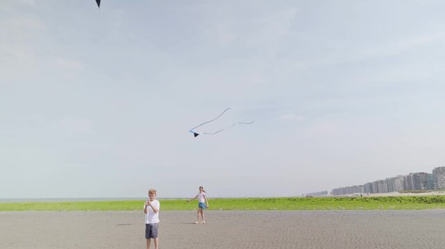 Boy and girl flying kites on a wide beach near coastal buildings children by the sea