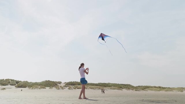 Girl flying a blue kite at a sandy beach sand dunes and the blue sky