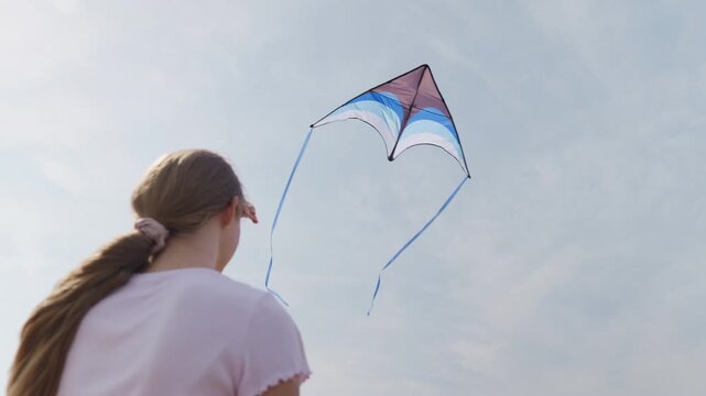 The girl looks up at the kite slow motion rear view close-up from below