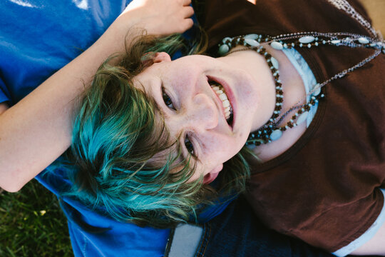 A happy young woman with green hair smiles up at the camera