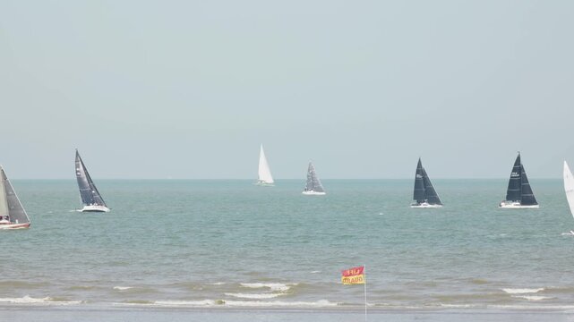 Sailing yachts offshore with a lifeguard flag in the foreground view from the beach