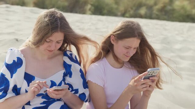The girl looks at phone and squints her eyes slow motion teenage daughter is sitting on the beach with her mother medium shot