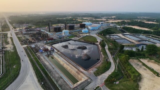 Aerial view of an industrial oil refinery plant with large storage tanks, piping systems, and processing facilities under a glowing sunset sky. Energy, fuel production, and industry concepts.