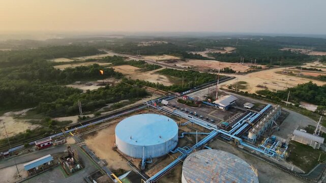 Aerial view of an industrial oil refinery plant with large storage tanks, piping systems, and processing facilities under a glowing sunset sky. Energy, fuel production, and industry concepts.