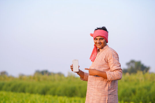 young indian farmer showing smartphone screen standing at green turmeric field
