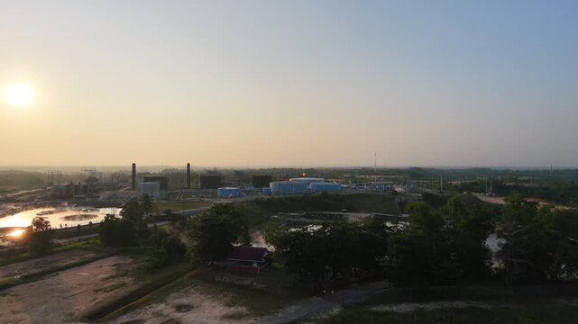 Aerial overview tracking across a sprawling oil and gas refinery plant under a hazy horizon. Highlights large industrial tanks, processing facilities, and complex technical piping.