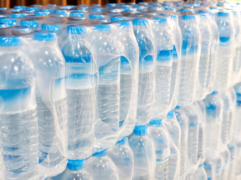 Close-up of stacked shrink-wrapped packs of bottled drinking water with blue caps. Ideal for beverage industry, wholesale, logistics, emergency supply, and stock concepts.