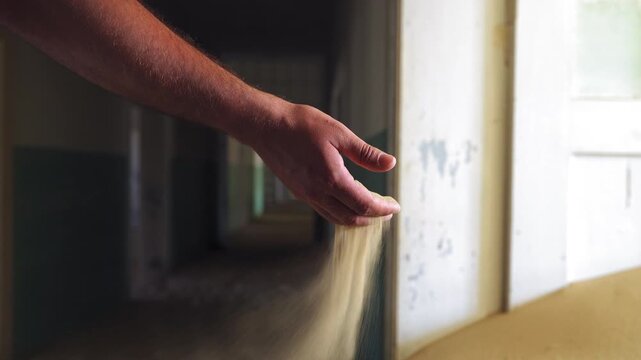 Hand slowly releases sand, Kolmanskop ghost town, Namibia. Close-up shot inside ruined house. Light enters through doorways. Cinematic stock footage.