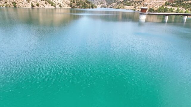Flight cruises very low about the aquamarine lake surface, tiny ripples, water intake structure, and then towards steep pine clad hills. Castril Granda Spain