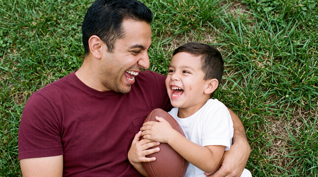 A father and son laugh while hugging a football on fresh grass, adding authentic game day family joy to party invitations and flyers.