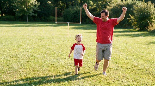 A father and son celebrate a touchdown run toward a backyard goalpost, ideal for energetic football game day party banner designs.