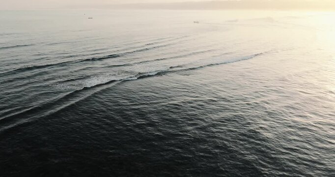 Aerial view of Plengkung Beach with gentle waves rolling onto the shore during the golden hour in Tegaldlimo, East Java, Indonesia.