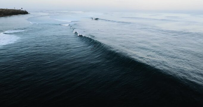 Aerial view of Plengkung Beach with surfers riding long waves in the ocean at Tegaldlimo, East Java, Indonesia.