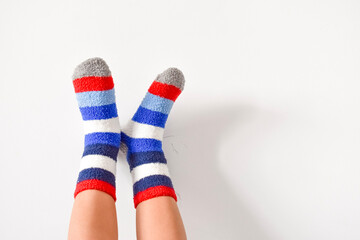 Child feet wearing bright colorful striped cozy fluffy warm socks raised up against clean white wall background indoor at home © Gulmira Uatkhanova