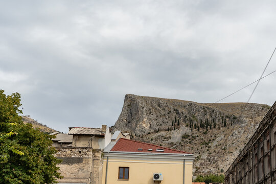 Scenic view of the rocky Velez mountain peak rising above traditional city roofs under a cloudy sky in Mostar