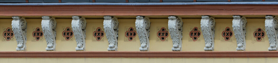 Cornice with decorative stucco brackets and sculpted leaf ornaments. Repeating quatrefoil motifs form an ornamental architectural frieze. © Frank