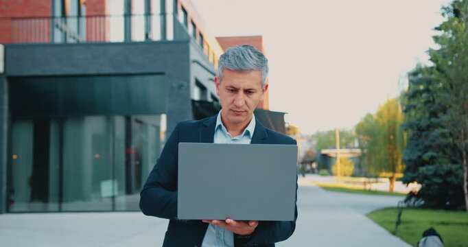 Portrait of a senior professional man working on a laptop outdoors, smiling with confidence as he types and analyzes data on the screen. Concept of remote work, digital entrepreneurship, and active