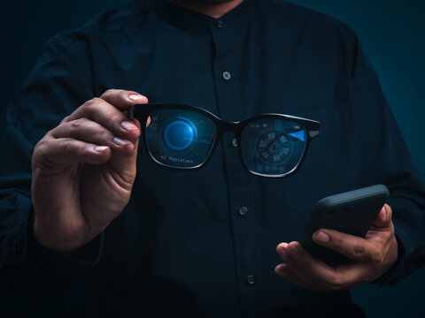 Businessperson holding futuristic AI smart glasses and smartphone with digital heads-up interface. Wearable artificial intelligence, contextual assistance, augmented reality, and connected technology.