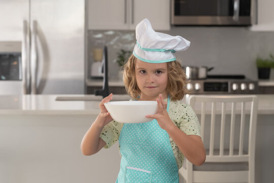 Chef kid boy baking on the kitchen. Child chef cook prepares food at kitchen. Kids cooking. Teen boy with apron and chef hat preparing a healthy meal.