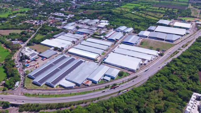 An aerial drone pan capturing a modern industrial park, large warehouses, and adjacent highway traffic in Tamboril, Santiago