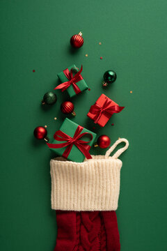 Merry Christmas stocking with wrapped gifts, red ornaments and ribbon for New Year celebration on vertical green copyspace