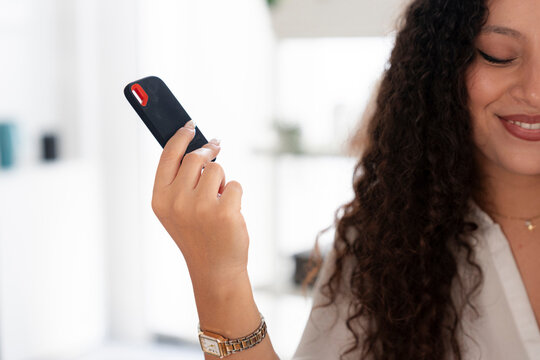 A young woman with curly brown hair holds a small portable solid state drive in her hand. She smiles while showcasing the compact tech accessory in a bright modern room.