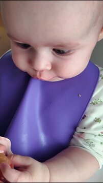 Cute 7-8 month old baby holding silicone teether in mouth while sitting at home. Concept of first baby teeth, teething discomfort relief, oral care development, sensory motor skills, and daily routine