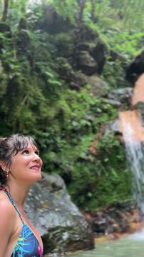 Woman relaxing in natural thermal pool waterfall environment