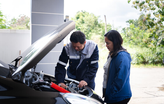 Asian mechanic repairing engine hood of car with female customer looking at repair process in garage workshop