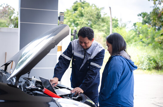 Asian auto mechanic using laptop computer to diagnose engine trouble for woman client at car repair shop