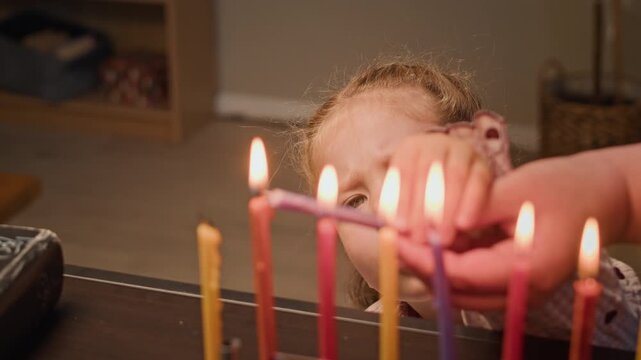 Caucasian child lighting Hanukkah menorah candles with parent assistance in close up. Footage suitable for Jewish holiday marketing, cultural heritage projects, and religious campaigns