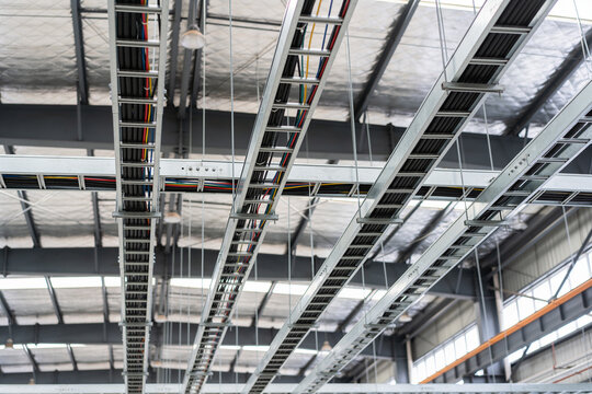 Industrial ceiling view featuring metal cable trays and electrical wiring in a large warehouse