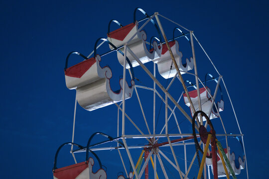 Small vintage Ferris wheel with red and white cabins illuminated against a deep blue night sky.