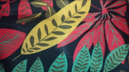 Close-up modern tropical leaf pattern printed on fabric texture with vibrant colors, featuring red, yellow, and green foliage designs on a dark background. Perfect for textile design, summer fashion b © adheart