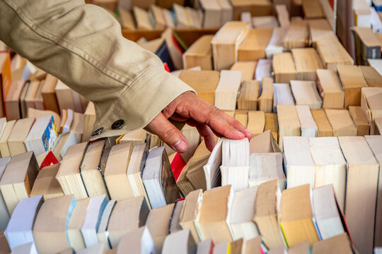 Gros plan de la main d'un client choisissant un livre dans le bac d'une librairie contenant beaucoup de livres d'occasion. Concepts de livres d'occasion et de diversit&eacute; de choix de lecture