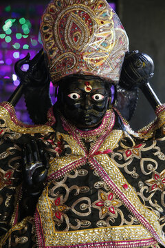 A black statue of Shani Dev holding a mace, wearing a crown and a gold-embroidered robe, in Delhi.