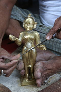 A craftsman in Vrindavan, India, is using a chisel to refine a brass statuette depicting the goddess Radha.