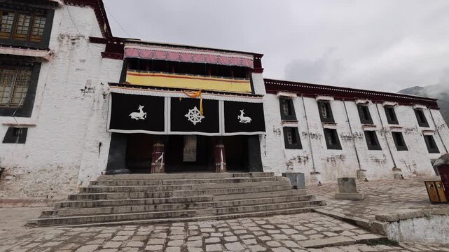 View of the historic Drepung Monastery with its white walls and traditional black banners featuring dharma wheels in Lhasa, Tibet, China.