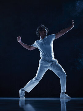 Determined cricket competitor lunging through bowling motion in dark blue studio. Athletic power, sporting performance concept.
