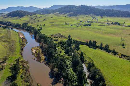 Aerial view of a winding river bordered by green farmland and wooded hills in Lambs Valley, Hunter Valley, New South Wales, Australia.