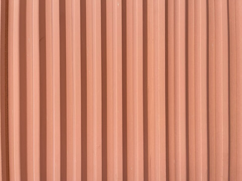 Close up of a pink corrugated surface with repeating vertical ridges, creating a minimalist geometric texture and modern architectural background.